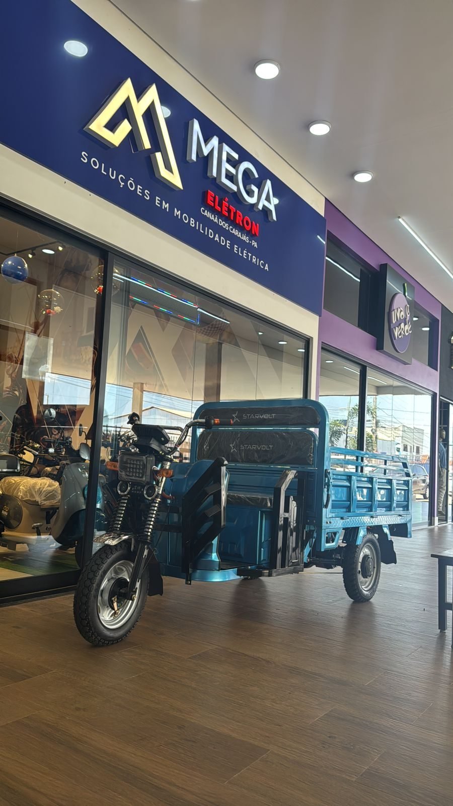 Fachada da unidade Mega Elétron em Canaã dos Carajás, Pará, com triciclo de carga em exposição.