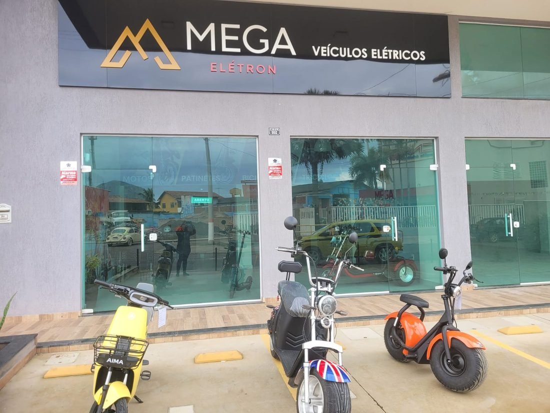 Fachada da unidade Mega Elétron em Maricá, Rio de Janeiro, com scooters elétricas coloridas expostas.